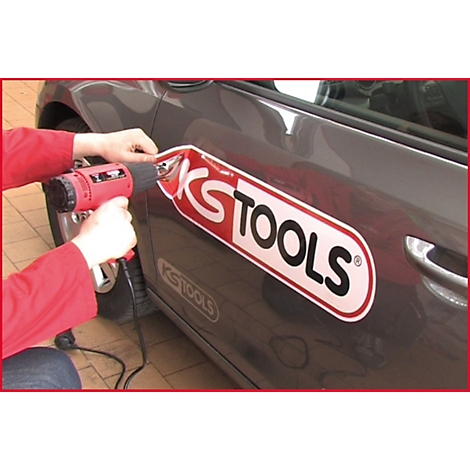 Person befestigt mit einem Heißluftföhn einen KS TOOLS-Aufkleber auf einem Autoteil.